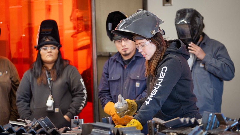 A woman gives a welding demonstration to students.